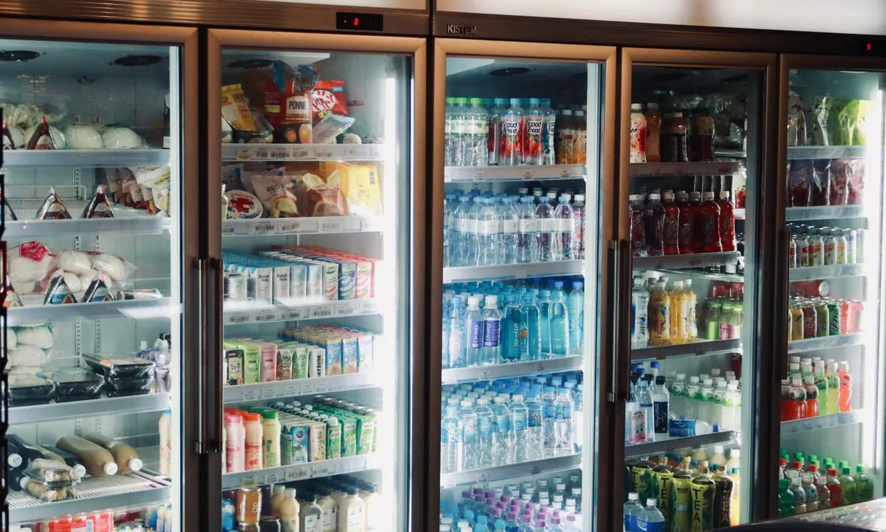 Geladeiras de portas de vidro de um supermercado, cheias de bebidas e alimentos refrigerados
