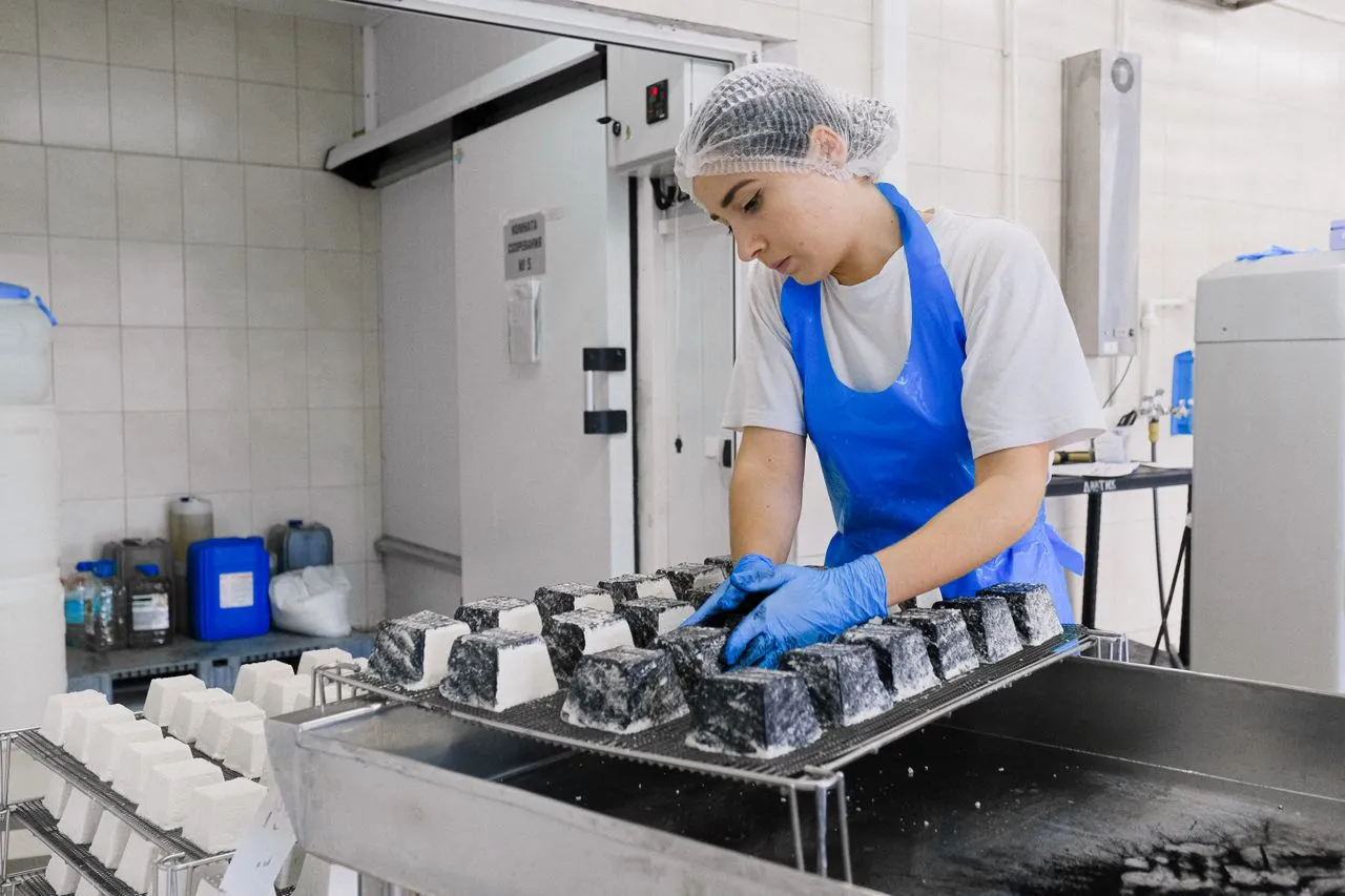 Operadora de touca e luvas organizando bandejas em uma linha de produção de alimentos