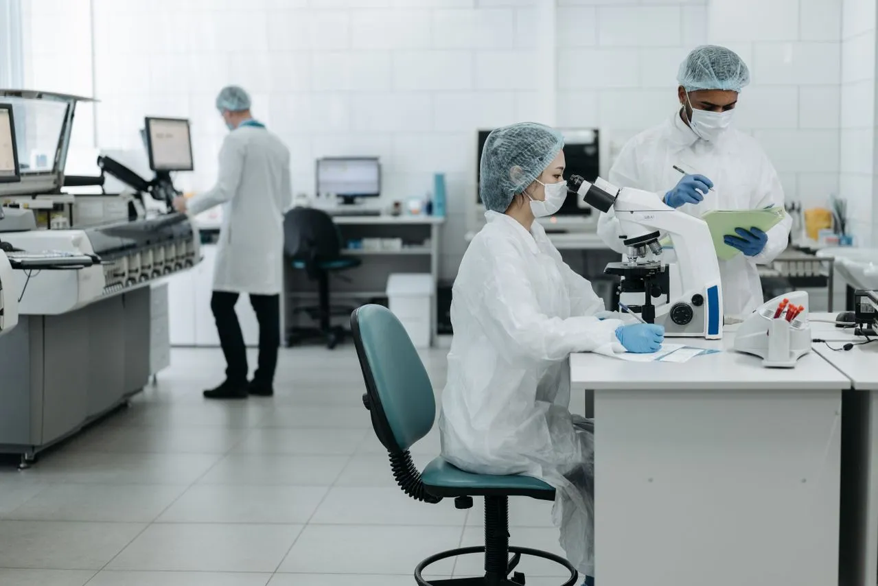 Técnicos de jaleco e touca trabalhando em um laboratório farmacêutico